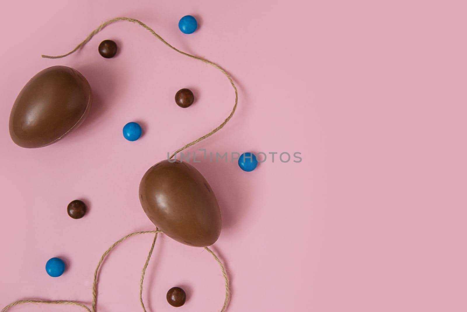 Flat lay composition with chocolate Easter eggs and chocolate sweets on pink background. View from above, empty space for text.