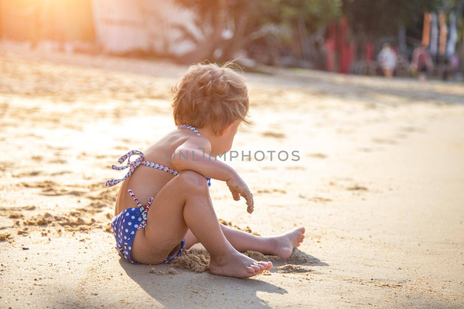 little girl sitting on a sandy beach in the sun by Mariaprovector