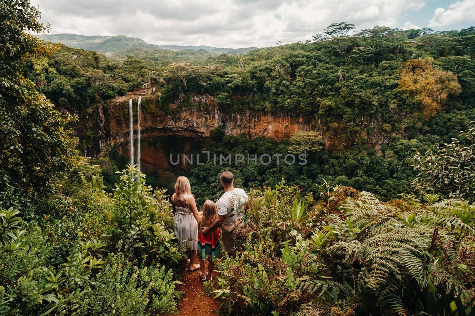 a family, a man, a woman and a daughter, stand on the edge of a cliff near a waterfall in Chamarel Park on the island of Mauritius.A couple with their daughter in the jungle of the island of Mauritius looks at a large waterfall falling down