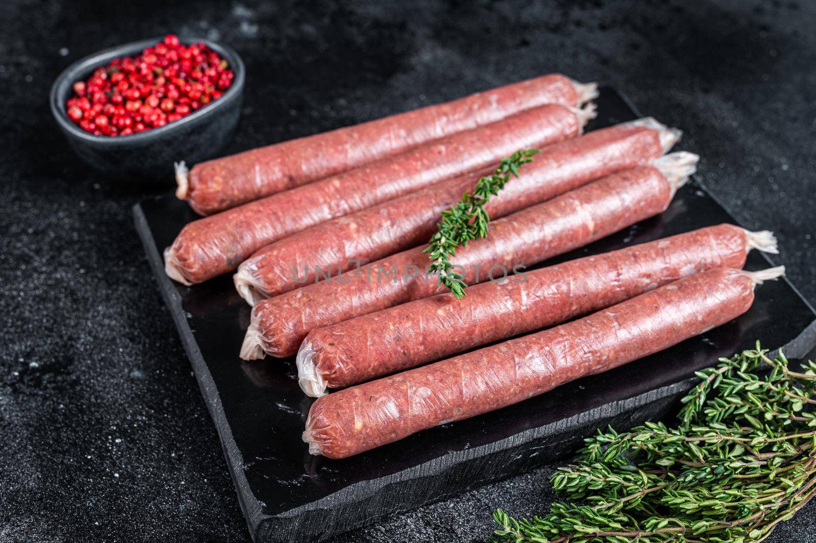 Fresh Raw butchers sausages in skins with thyme on marble board. Black background. Top view.