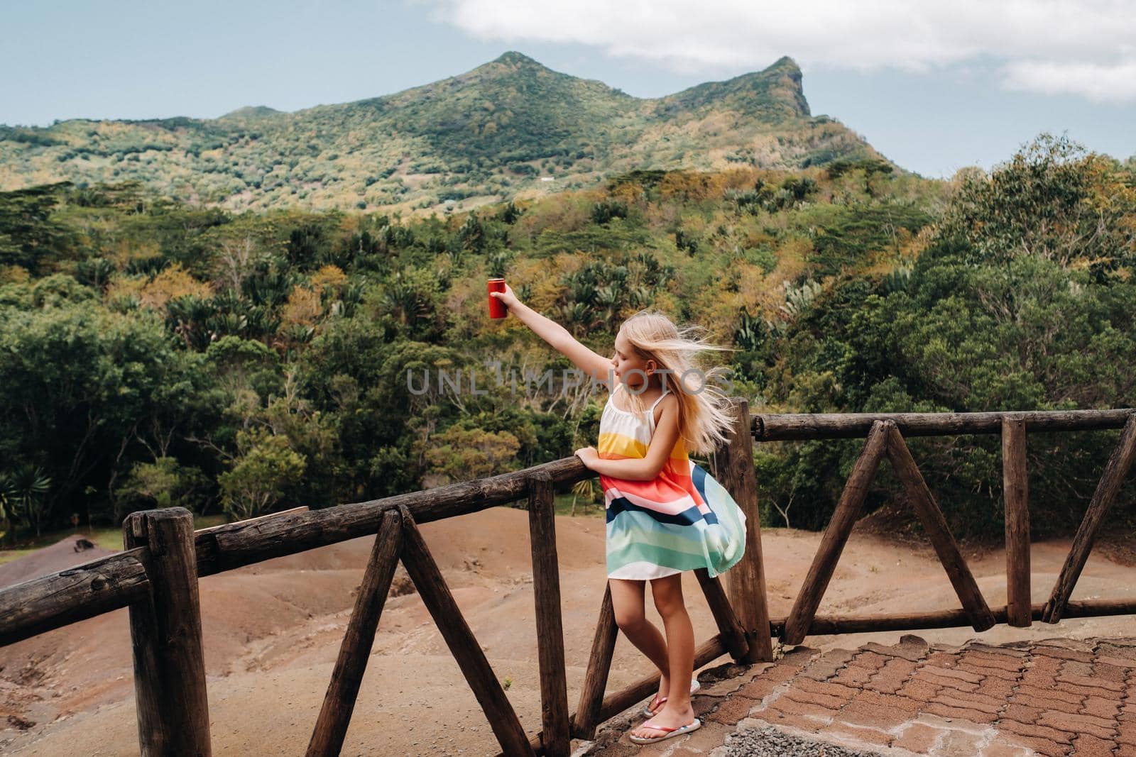 a little girl with a red can of drink in her hands against the background of the mountains of the island of Mauritius, nature reserve, Chamarel Sands.Mauritius island by Lobachad