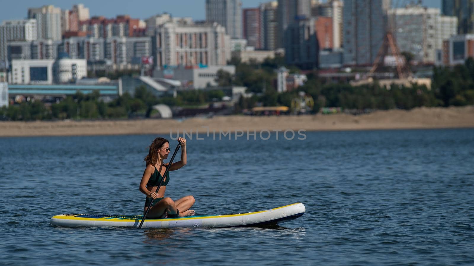 Caucasian woman is riding a SUP board on the river in the city. Summer sport. by mrwed54