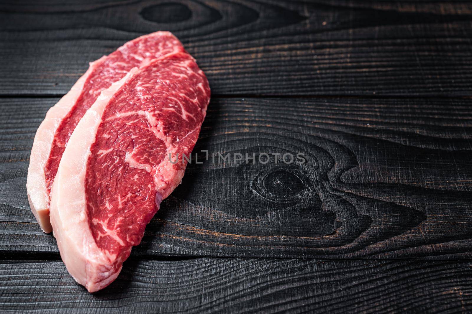 Raw rump steak or top sirloin cap beef meat steaks on butcher table. Black wooden background. Top view. Copy space by Composter