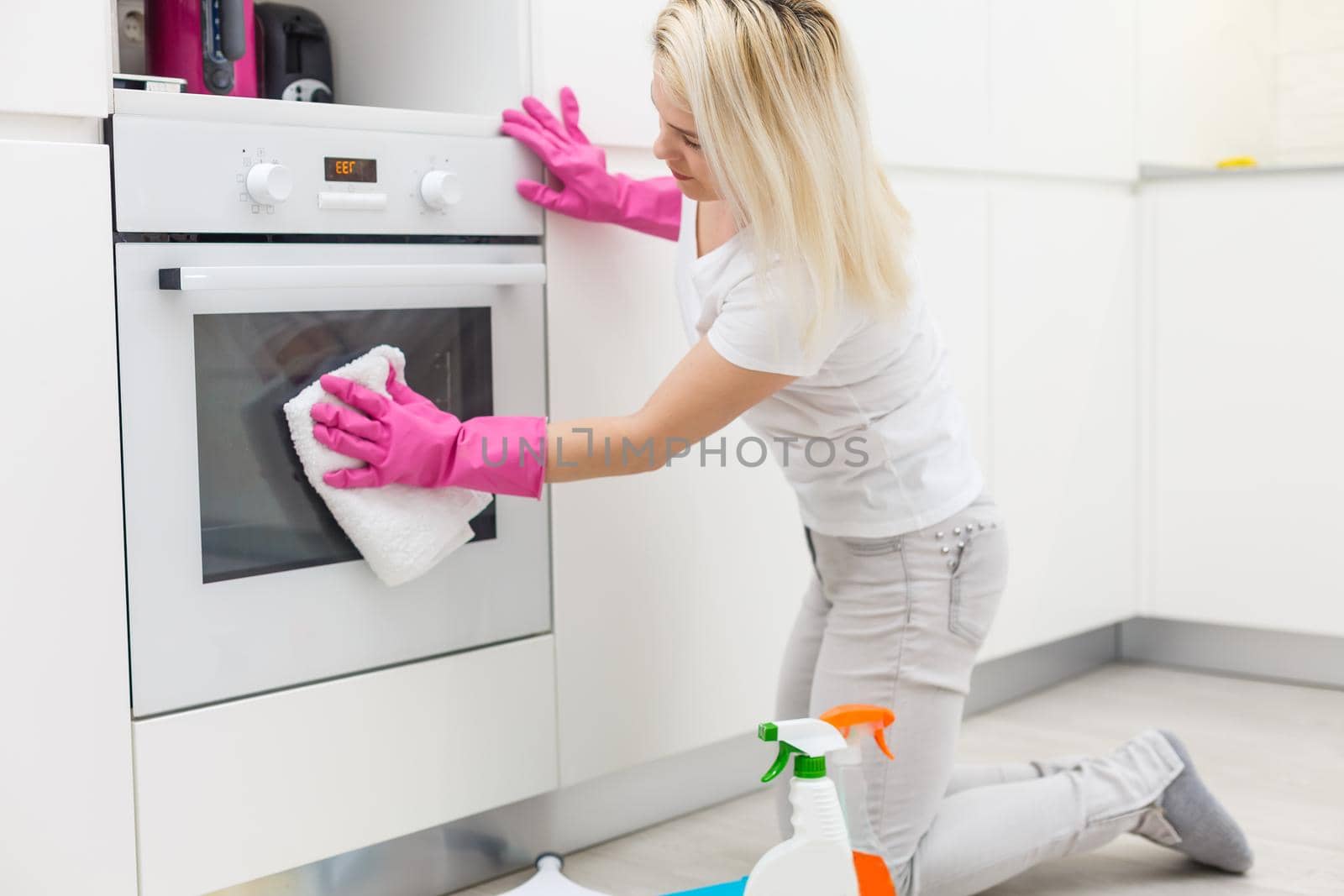 Woman in the kitchen is smiling and wiping dust using a spray and a duster while cleaning her house, close-up by Andelov13