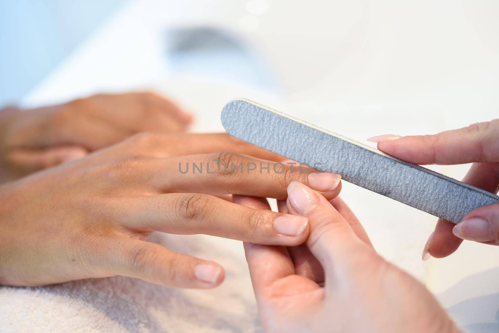 Woman in a nails salon receiving a manicure with nail file by javiindy