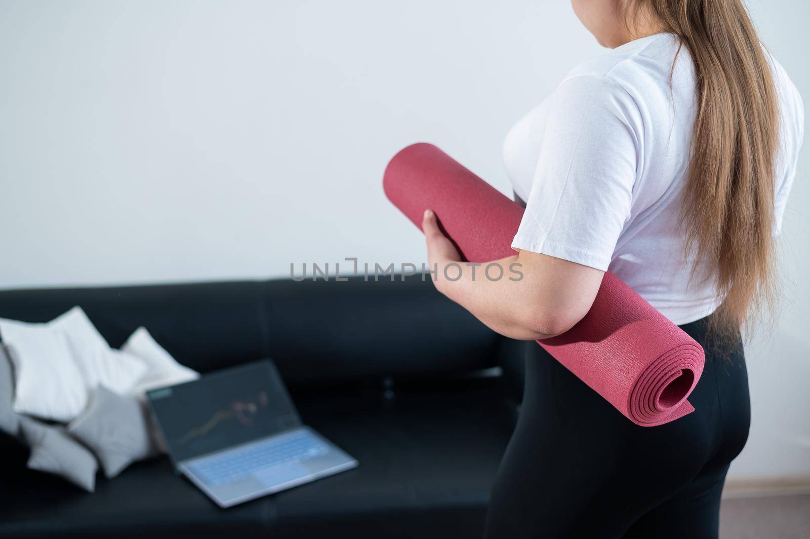 Young chubby woman folds sports mat after online fitness class.