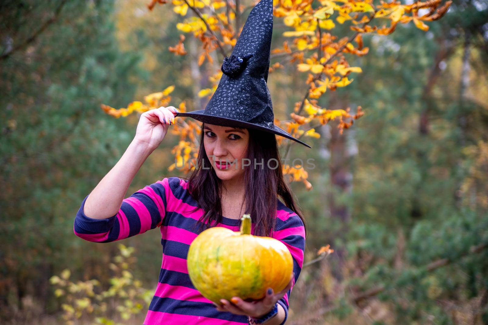 beautiful wonam in a witch costume with a pumpkin in the forest. Background happy Halloween Holiday