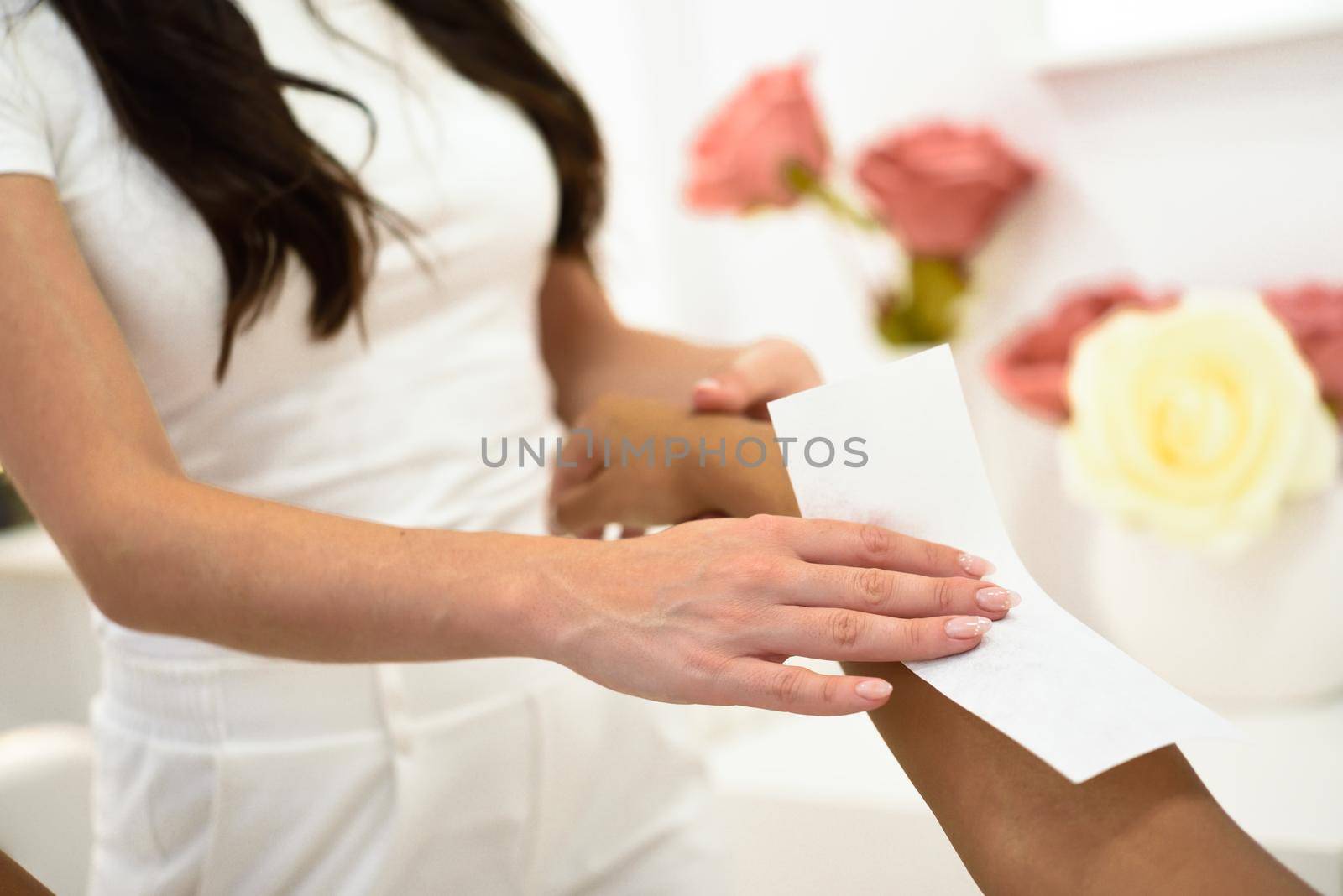 Woman having hair removal procedure on arms applying wax strip depilatory in salon. Depilation concept