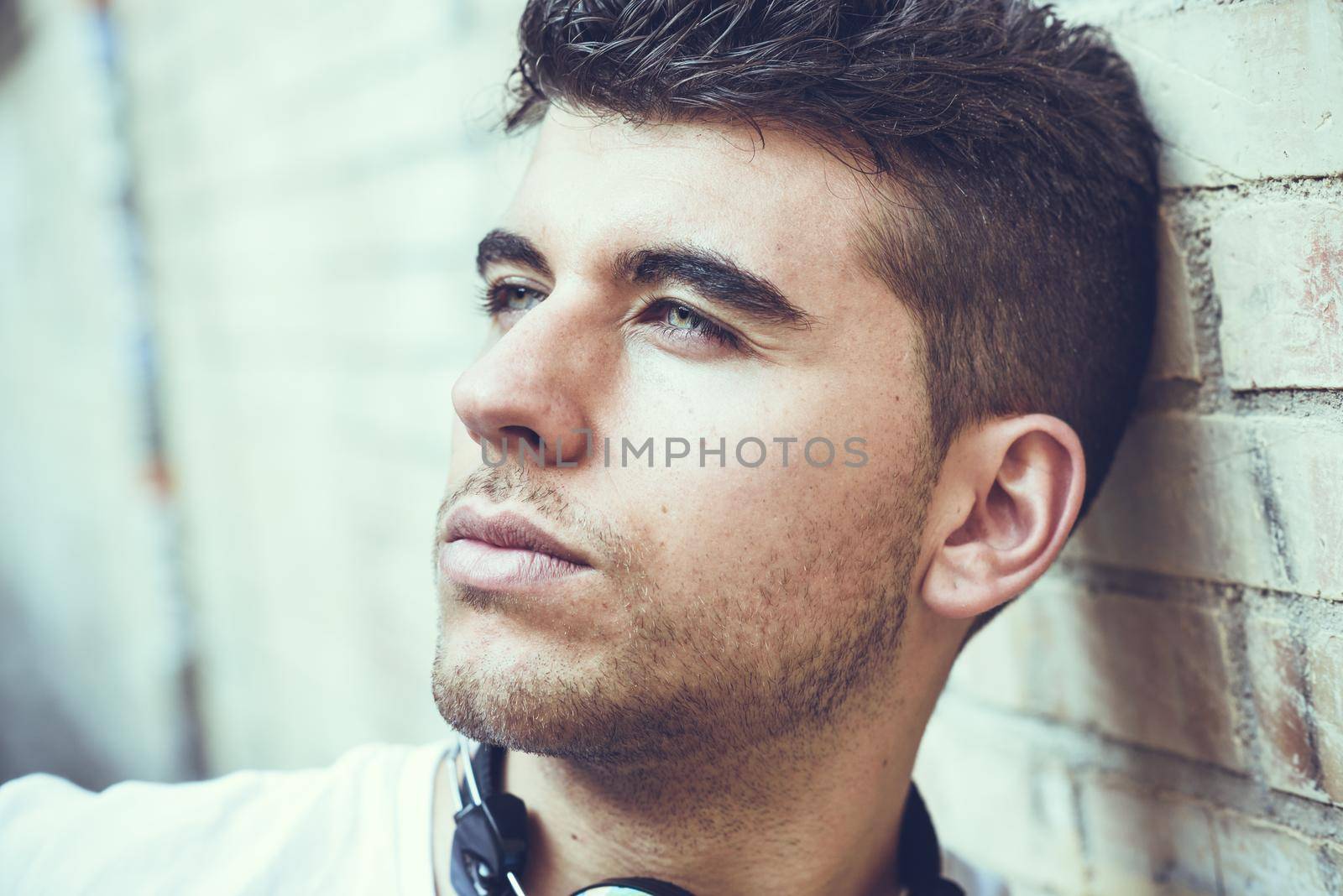 Close-up portrait of a young man with blue eyes posing near a wall. Model of fashion in urban background wearing white t-shirt
