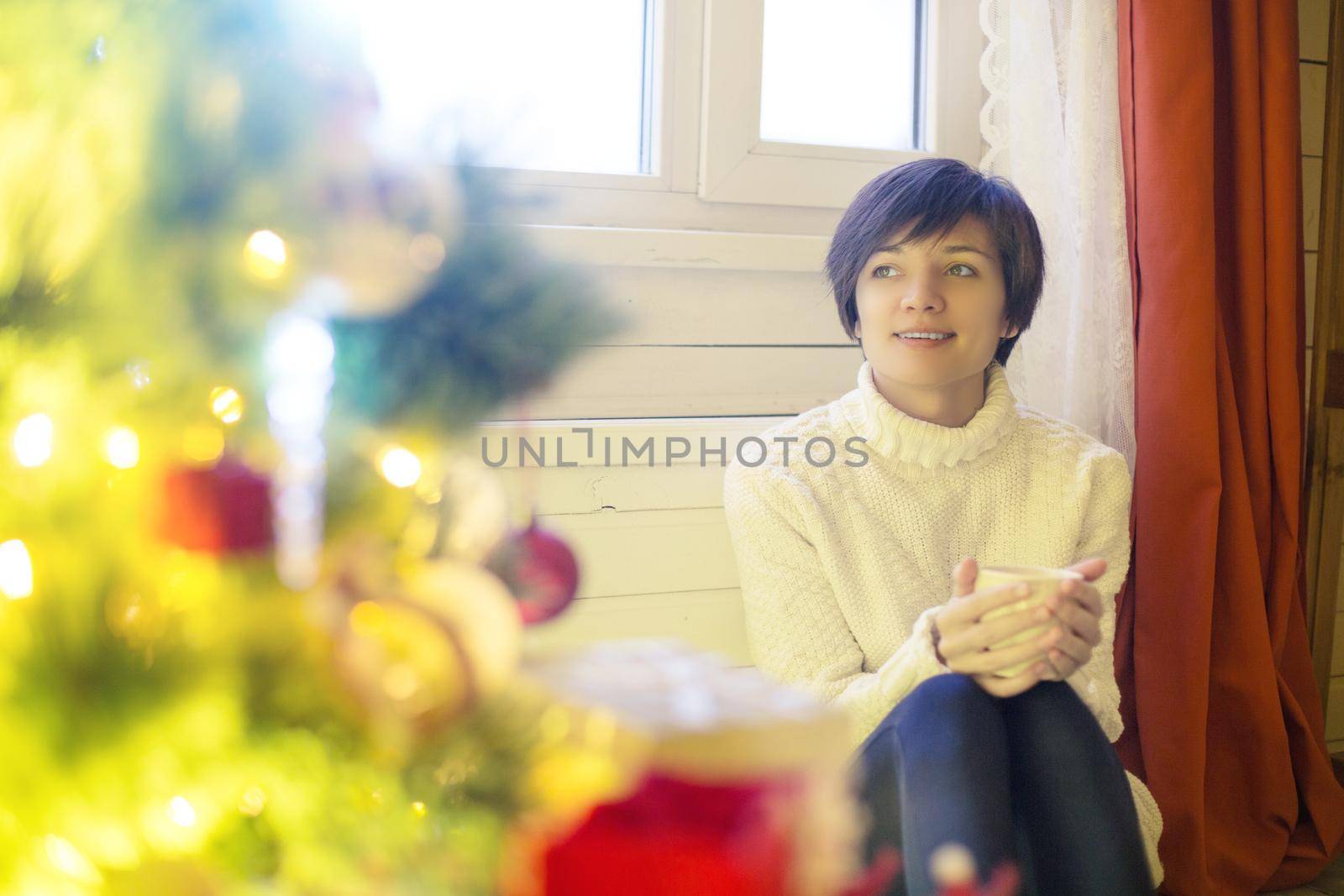 Smiling young woman with cup of hot chocolate in front of Christmas lights.