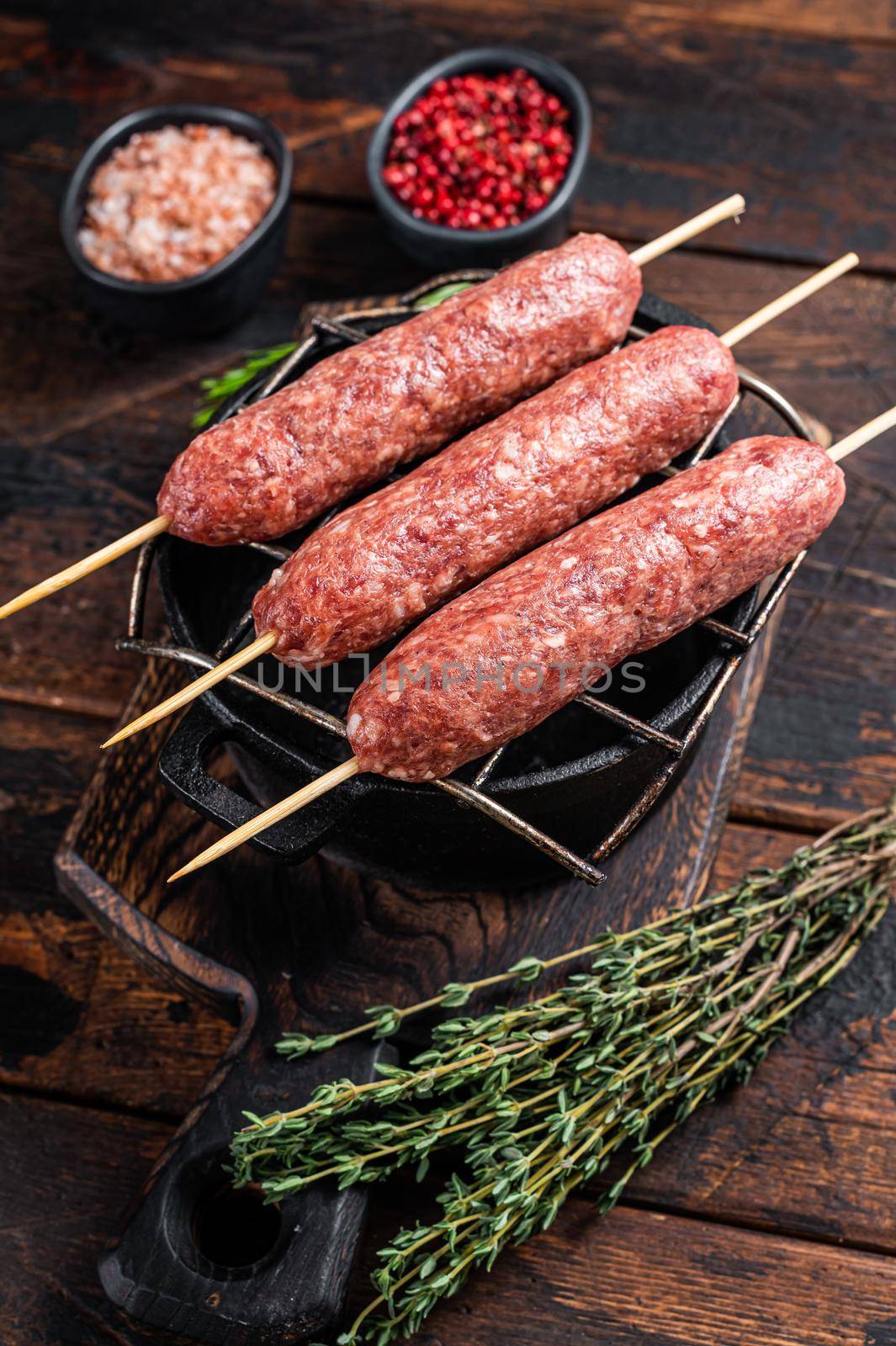 Raw kofta or lula kebabs skewers on a grill with herbs. Dark wooden background. Top view.