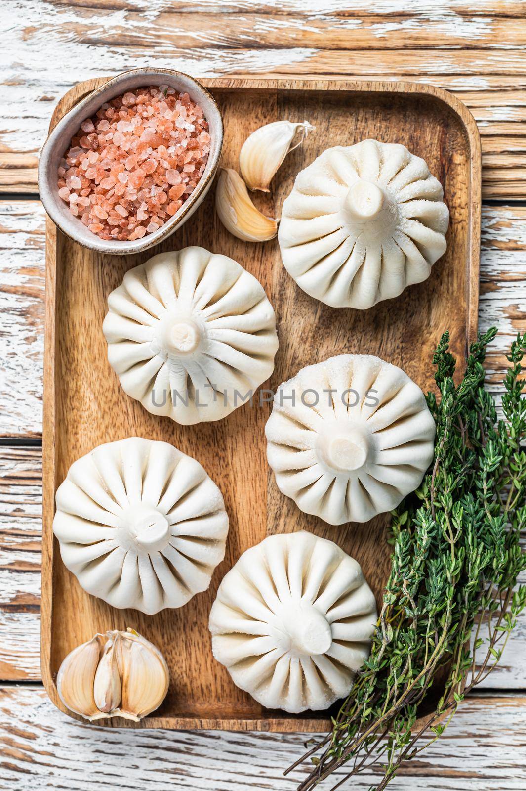 Frozen Raw dumplings Khinkali with beef and lamb meat on wooden tray with herbs. White wooden background. Top view.