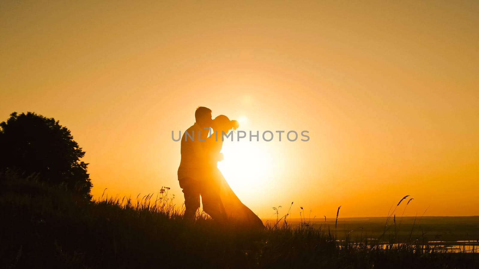 Young loving couple - brave young man and beautiful girl at sunset silhouette, kissing, telephoto shot