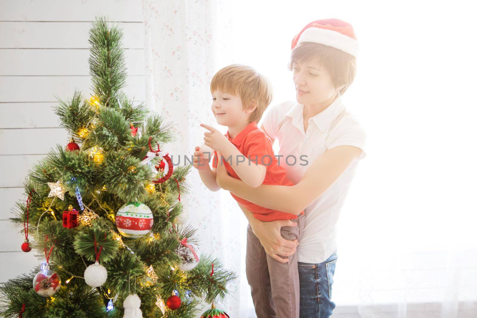 Mother with her son on hands decorating Christmas tree together.