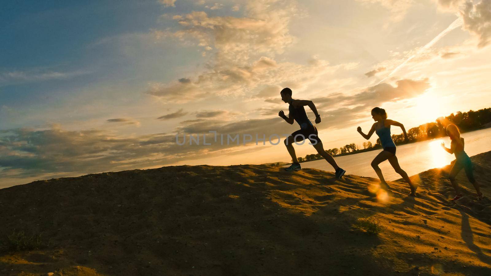 A group of athletes - two girls and a guy are fleeing the mountain, near river at dusk, silhouette