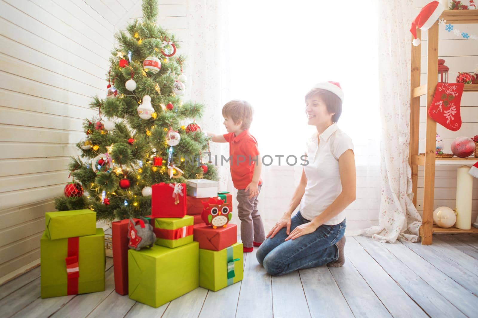 Smiling mother with her beautiful little son decroating Christmas tree with baubles at home.