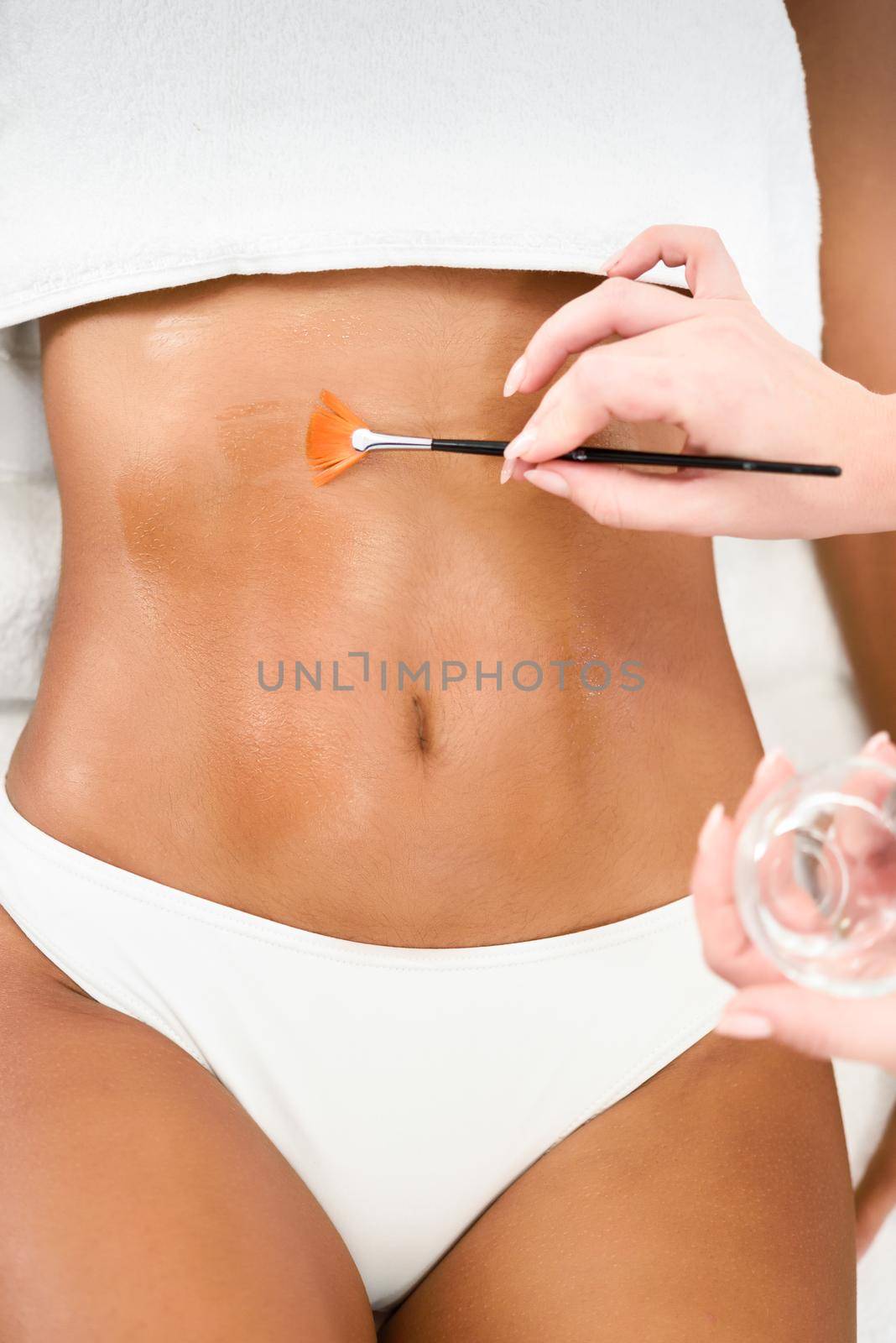 Woman receiving belly massage treatment with oil brush in spa wellness center. Beauty and Aesthetic concepts.