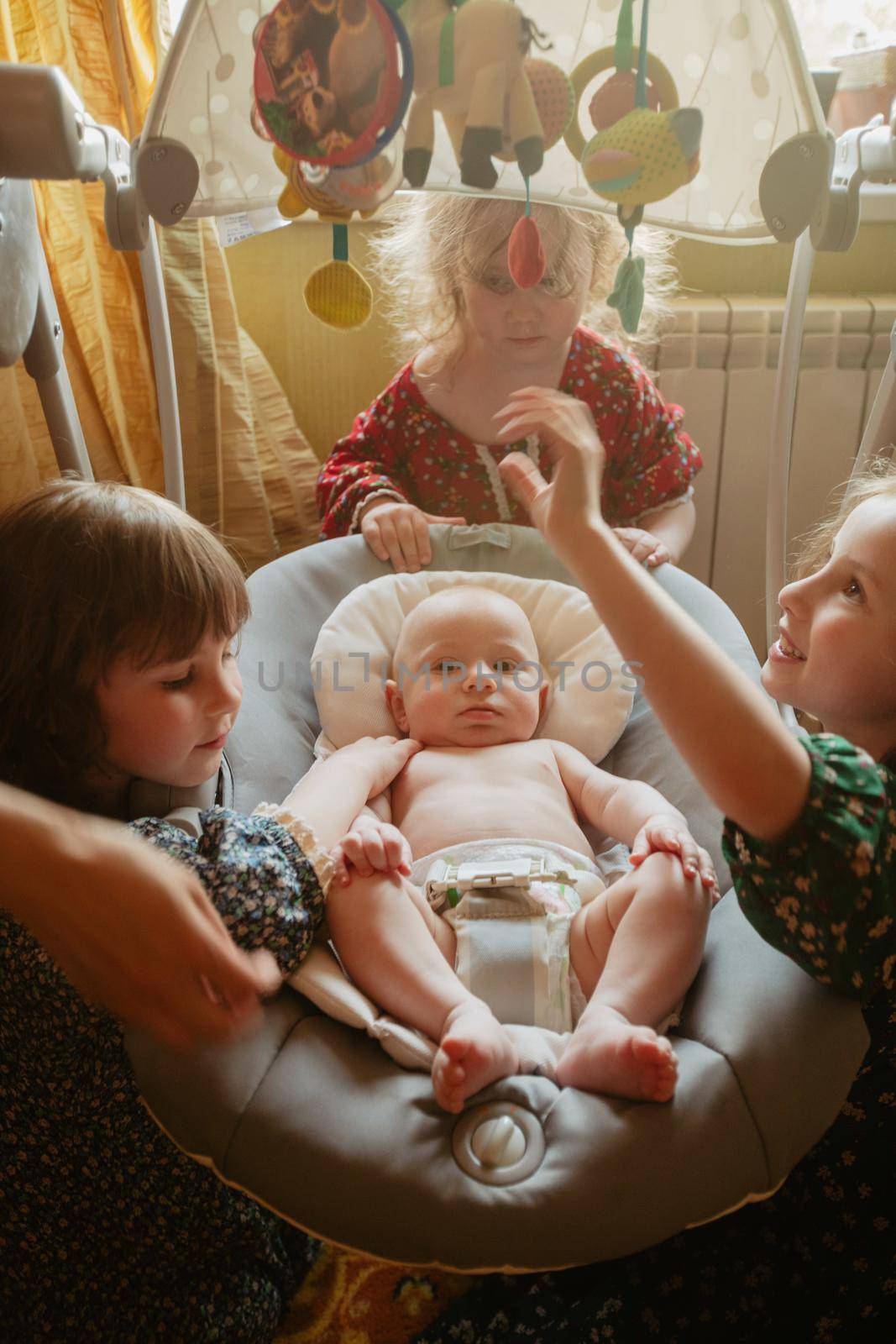 High angle of curious little girls gathering around sweet baby while playing together at home