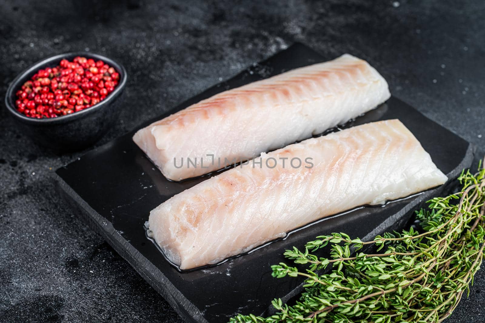 Raw cod loin fillet fish on marble board. Black background. Top view.