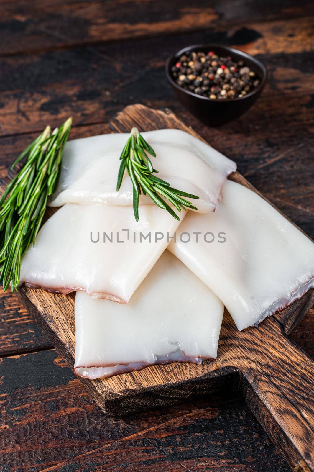 Raw Calamari or Squid on a wooden board with rosemary. Dark wooden background. Top view by Composter