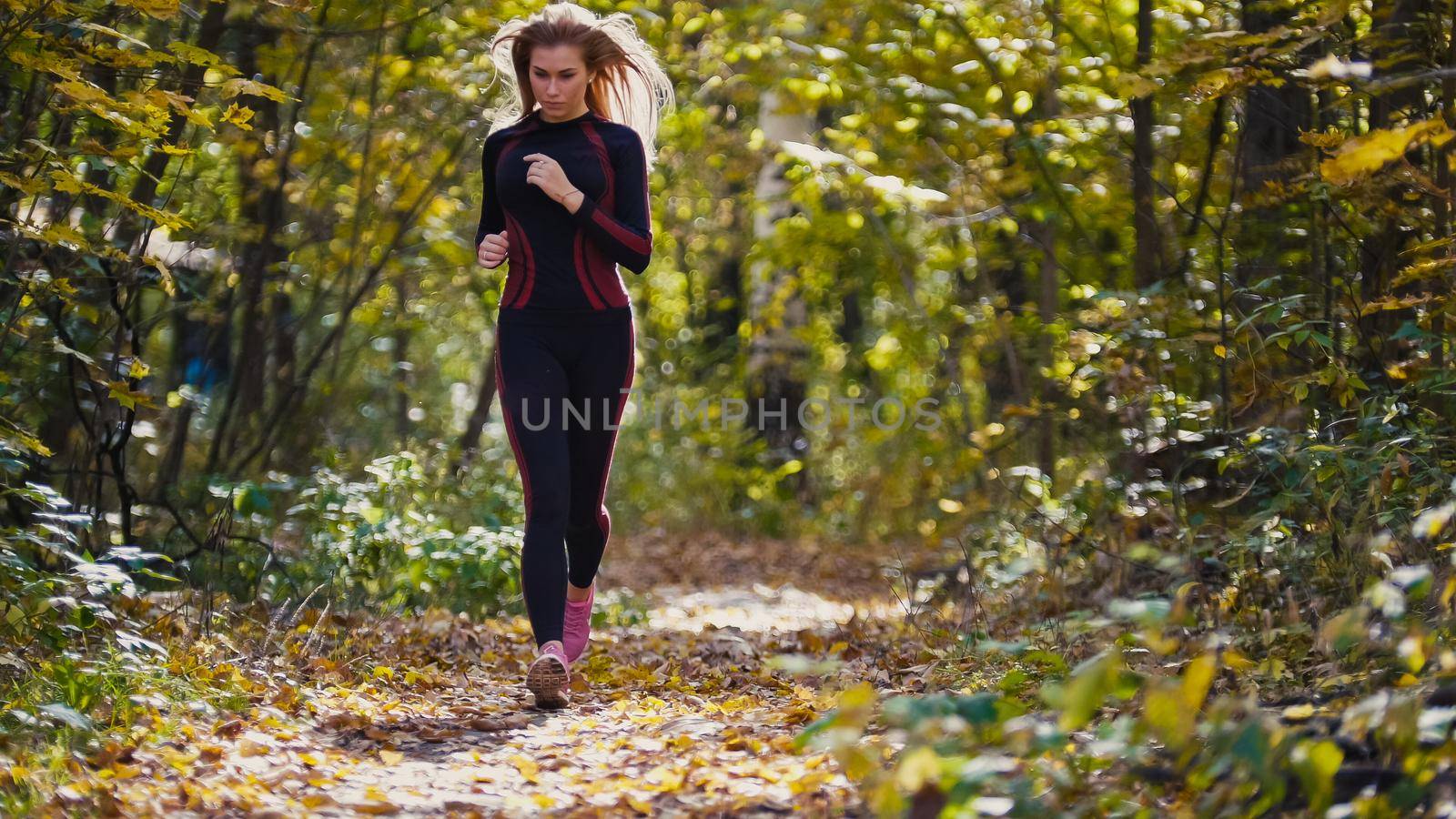 Young runner girl have jogging on autumn road covered with fallen leaves. Sports healthy lifestyle concept, telephoto