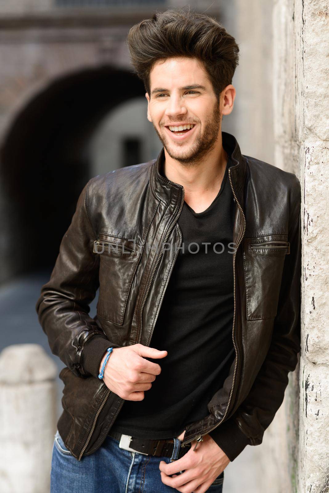 Portrait of a young handsome man, model of fashion, with modern hairstyle, smiling in urban background