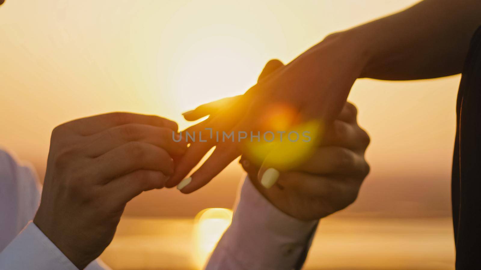 Wedding Ring Put On Finger Hands Touching Sunset Bride Groom Man Woman Marriage Proposal Vacation Honeymoon, horizontal, close up