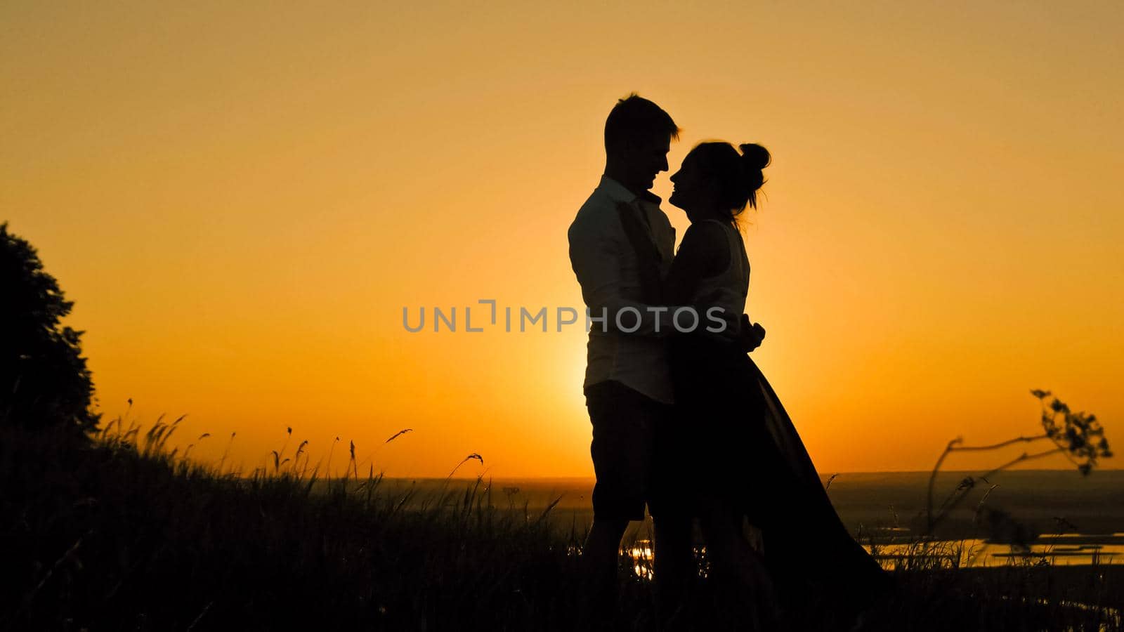loving couple - brave young man and beautiful girl stands on high hill at sunset have hugs kiss, silhouette, slider shot by Studia72