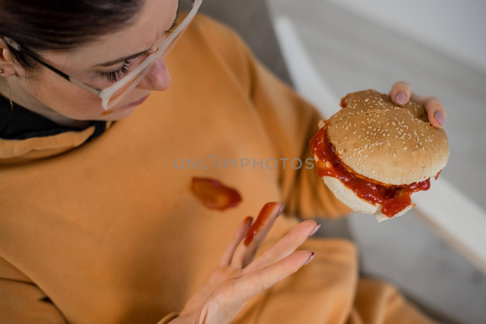 Caucasian young woman eating burger and getting dirty in ketchup. Sloppy girl by mrwed54