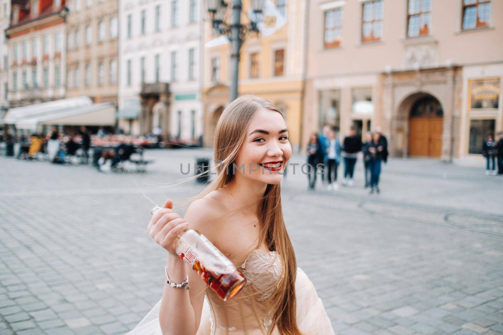 A bride in a wedding dress with long hair and a drink bottle in the Old town of Wroclaw. Wedding photo shoot in the center of an old Polish city.Wroclaw, Poland.