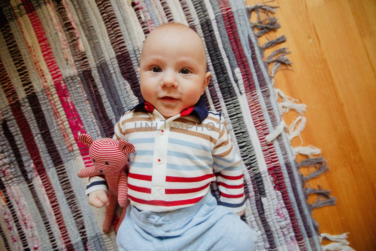 From above of cute smiling infant lying with toy on carpet and looking at camera