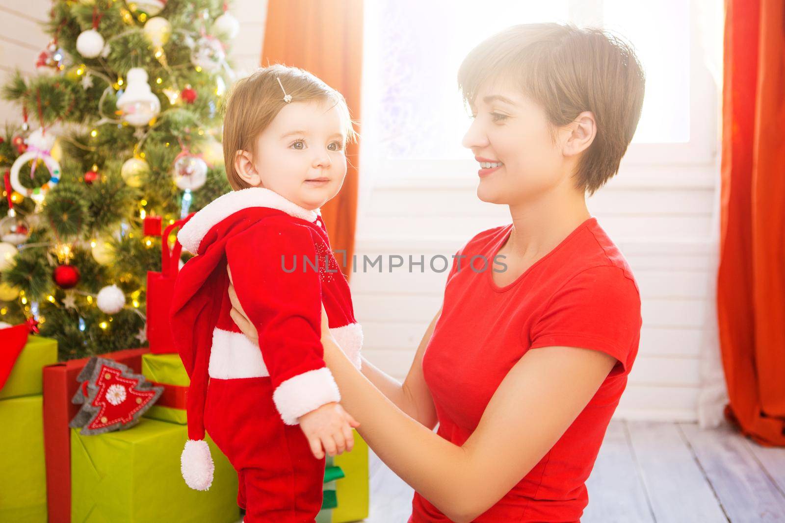 Beautiful young mother and daughter dressed as santa claus sitting on the floor over Christmas tree.