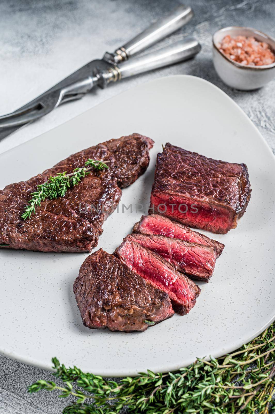 Roasted sliced rump beef meat steak on a plate with thyme. White background. Top view.