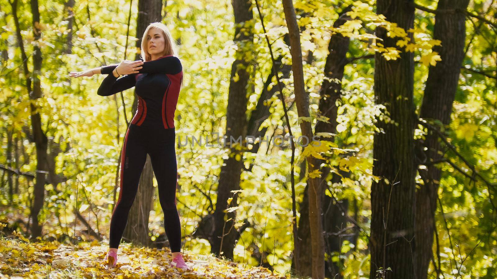Woman doing fitness exercises outdoor. Female stretching her shoulders in autumn forest. Slim girl at outdoor work-out - the right side, telephoto