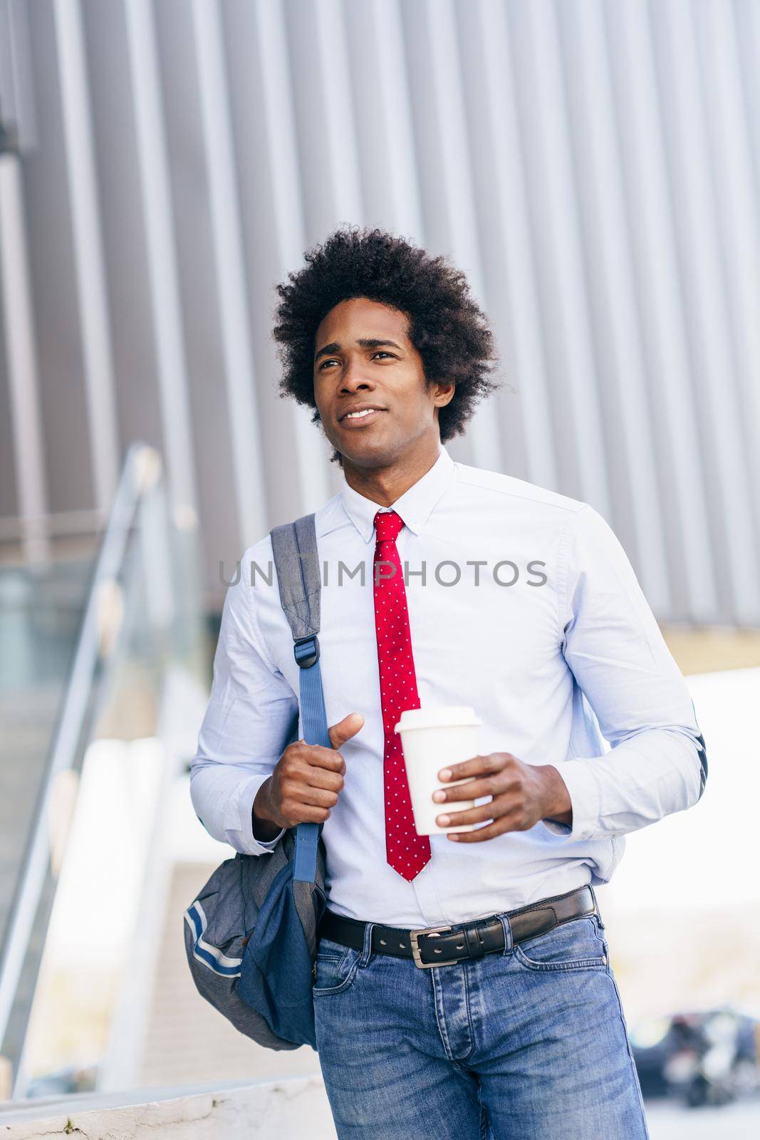 Black Businessman walking down the street with a take-away glass. Man with afro hair.