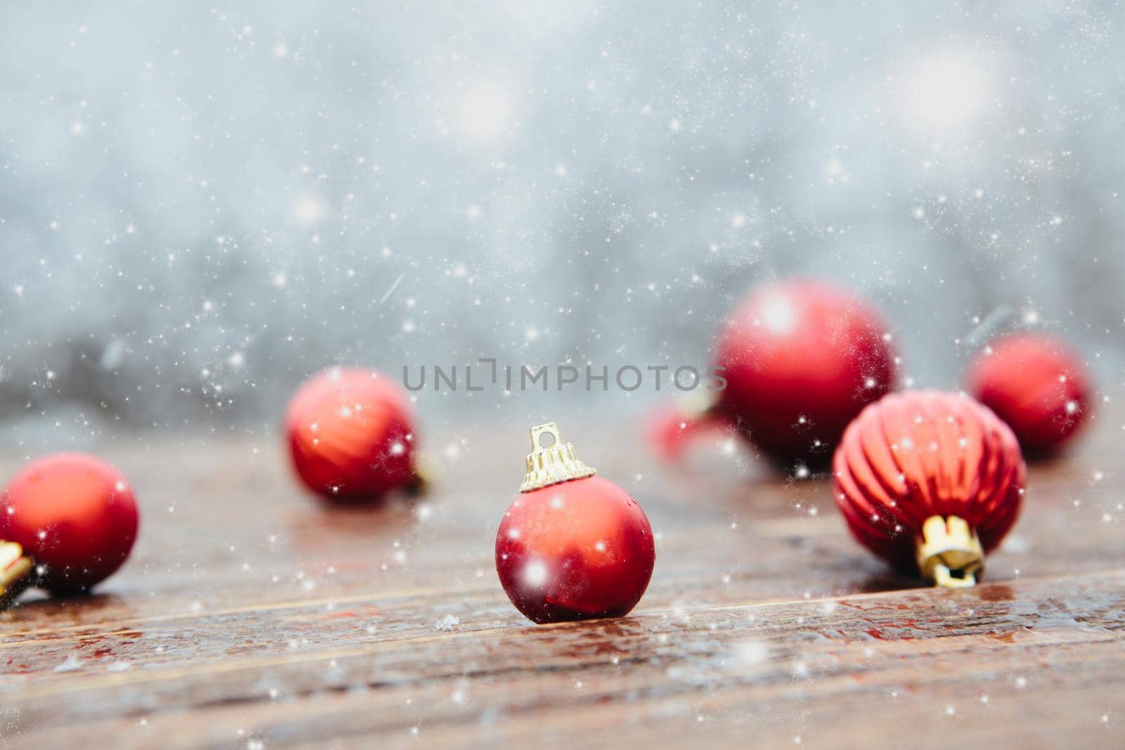 Red balls on board place snow and landscape of tree. Beautiful Christmas bauble decorations lie on the wooden table over snow covered forest background. Atmosphere of magic and fairy tales .