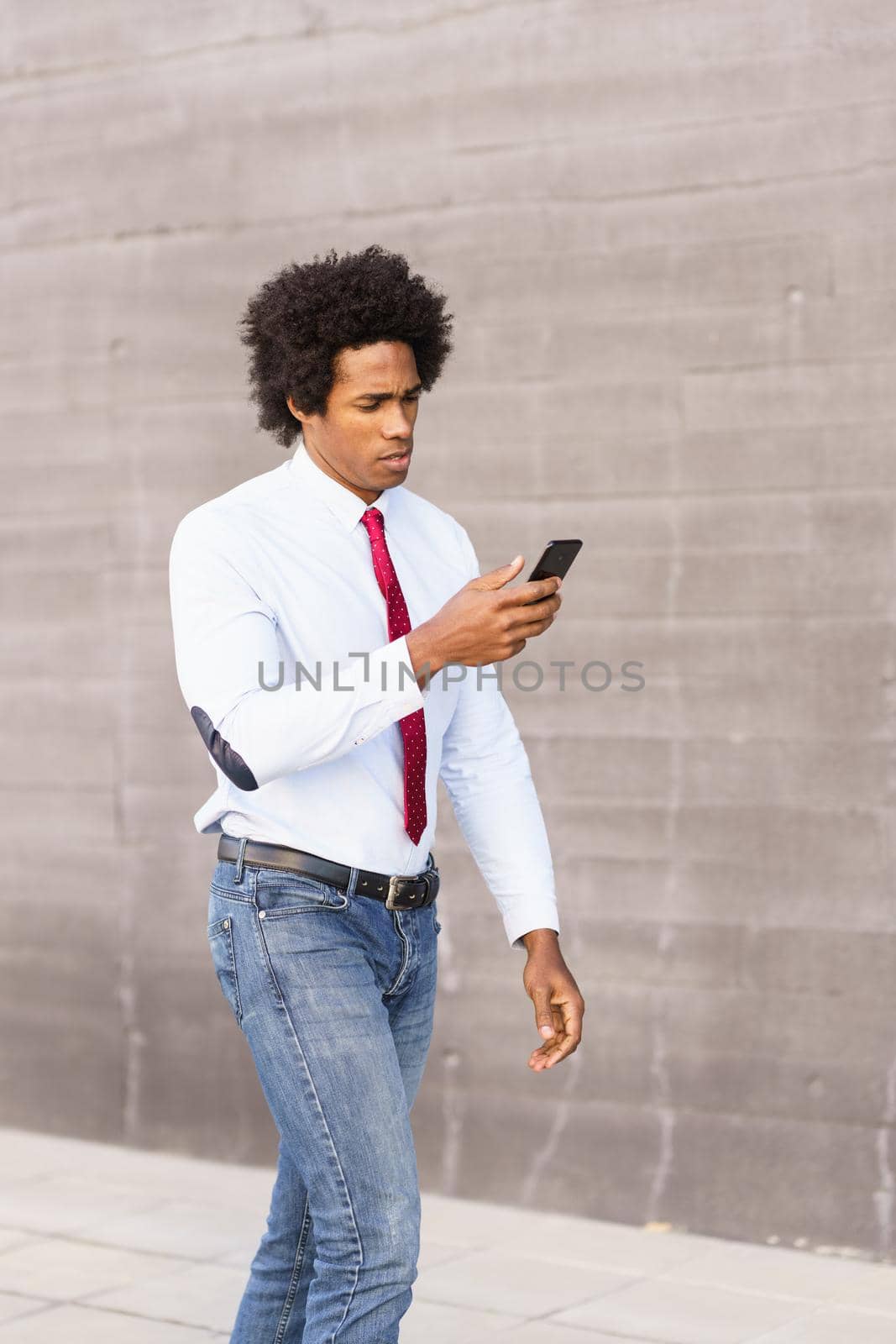 Black Businessman using his smartphone walking down the street.