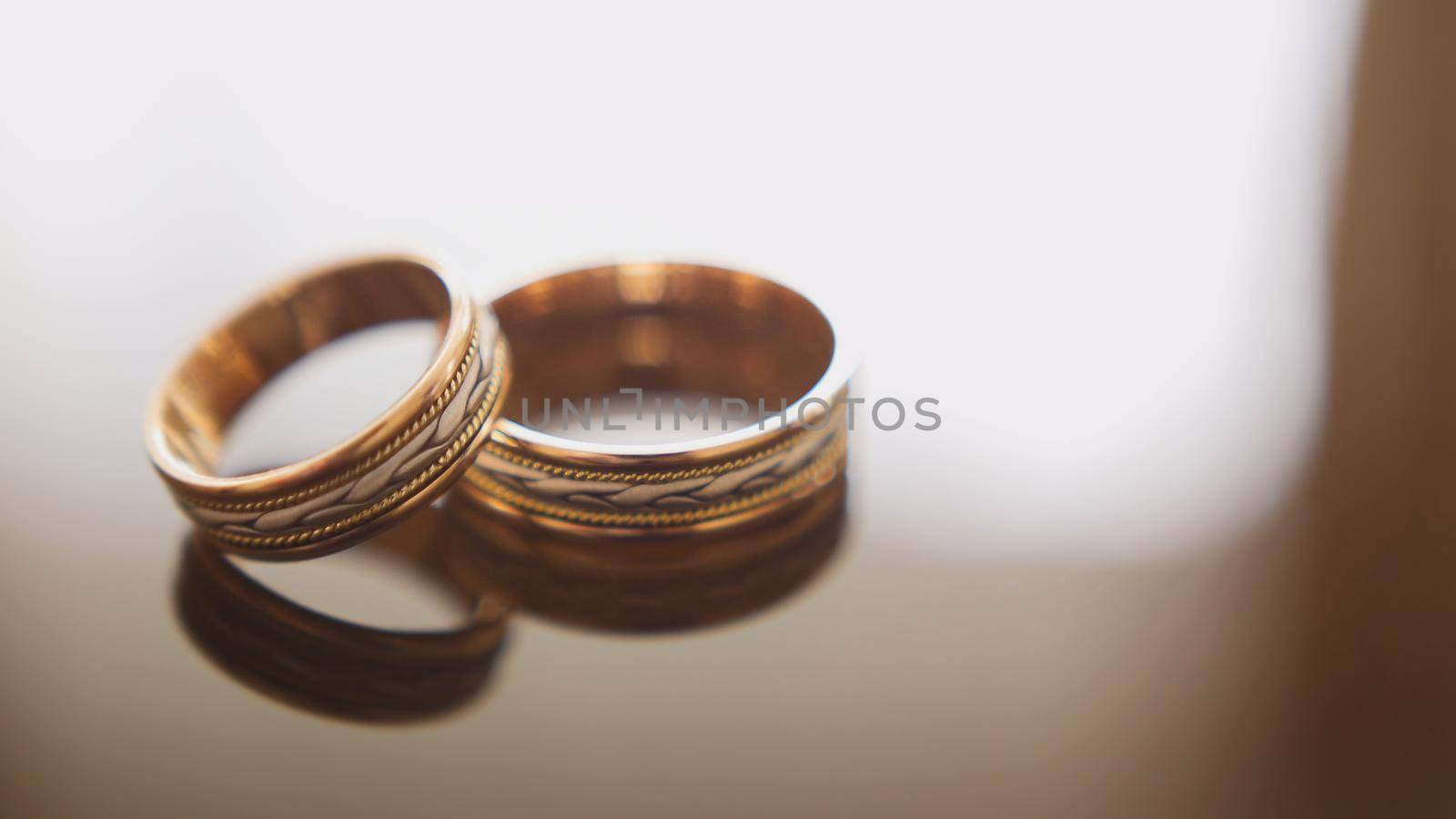 Golden wedding rings on mirror glasses table - one lies top of another, horizontal by Studia72