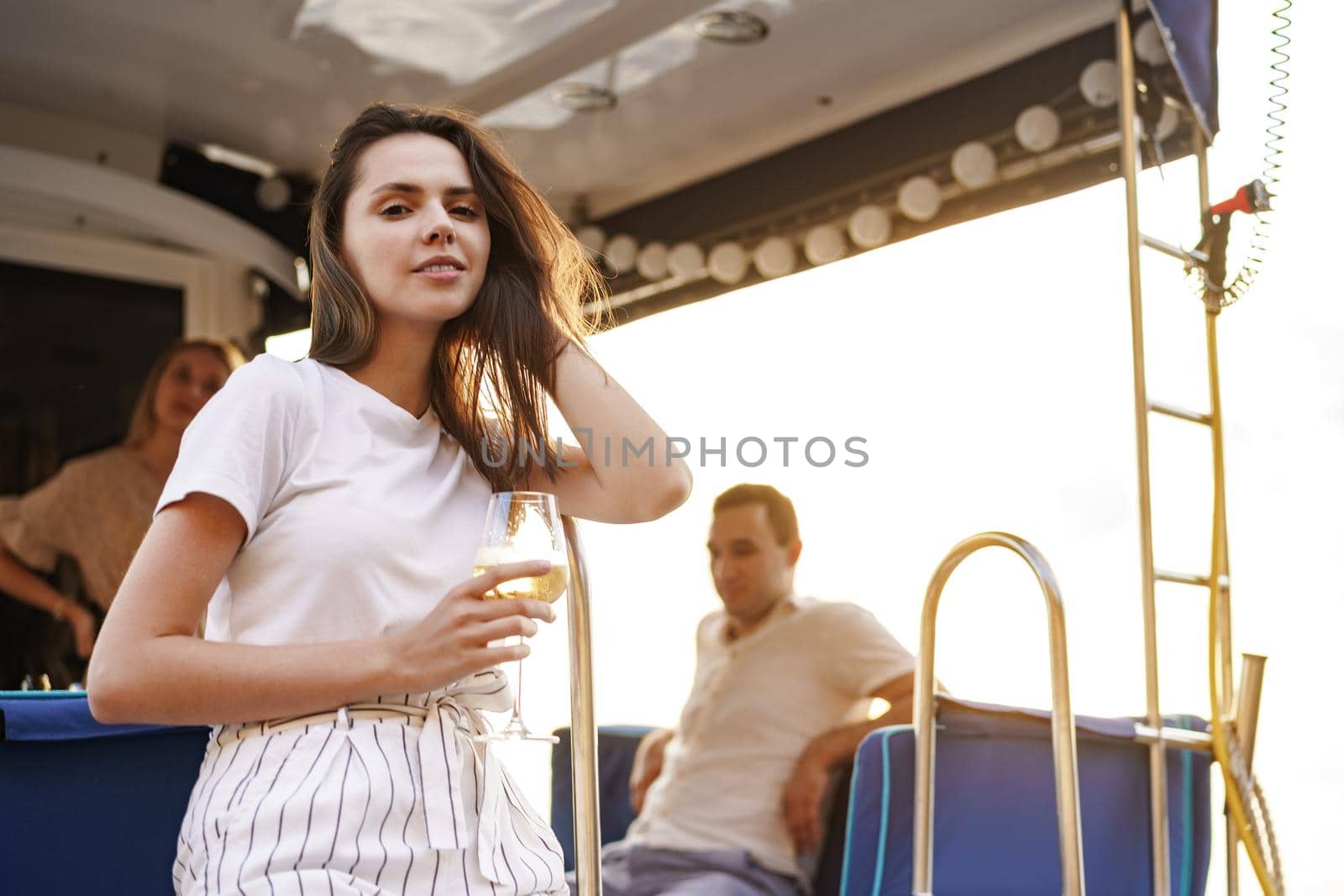 Young woman holding a wineglass and sitting on deck of sailing yacht boat