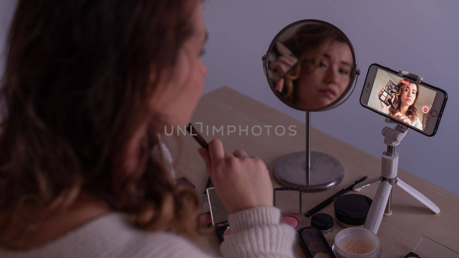 Caucasian woman leads an online make-up lesson for herself on her mobile phone.