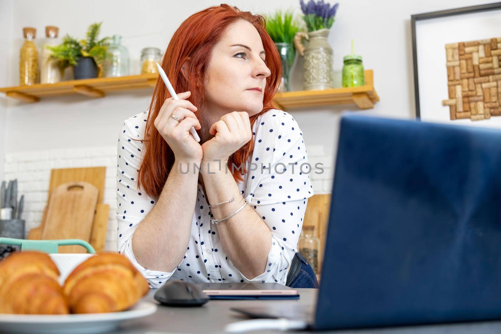attractive woman sits in front of a computer in the kitchen. blogger writes a post on the internet. content author, copyright specialist. creative imagination