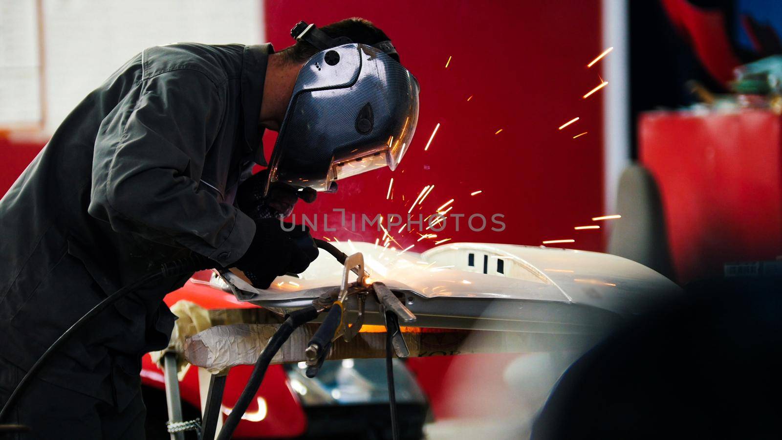 Welding industrial: worker in helmet repair detail in car auto service, telephoto