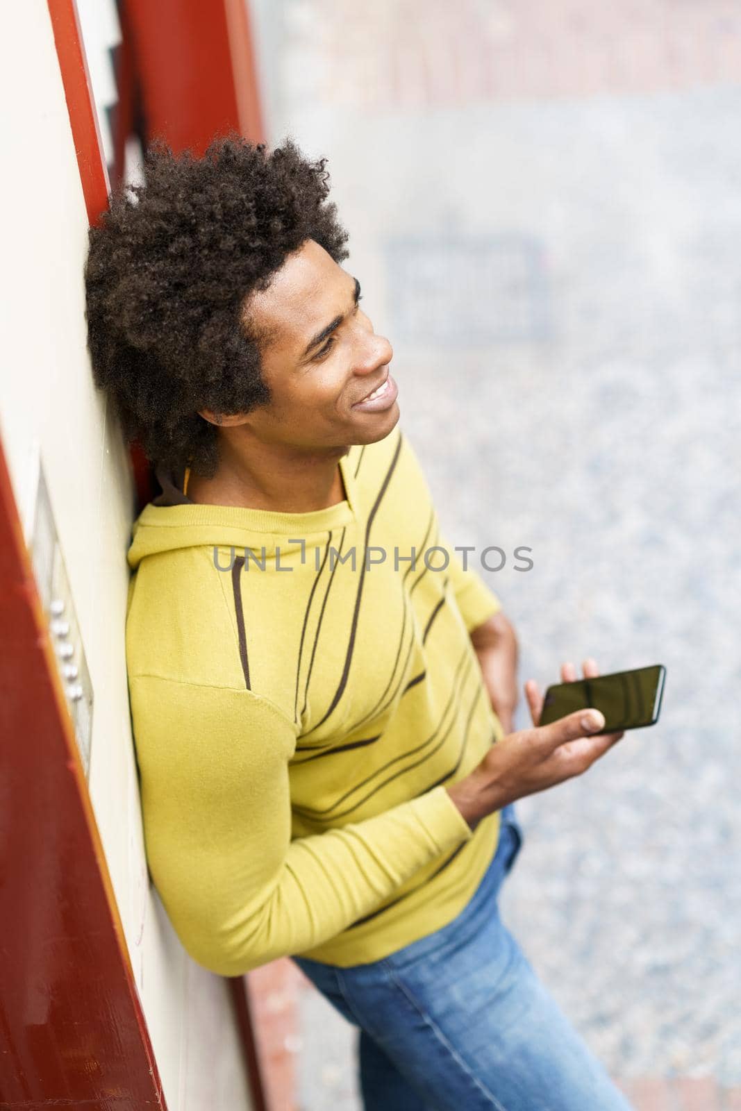 Black man with afro hair and headphones using smartphone in urban background.