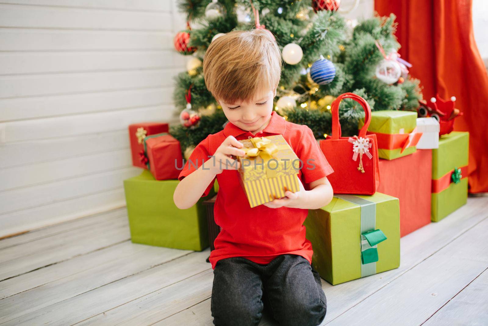 Cute little boy of about five year with a gift in a decorated Christmas room with a xmas tree. .