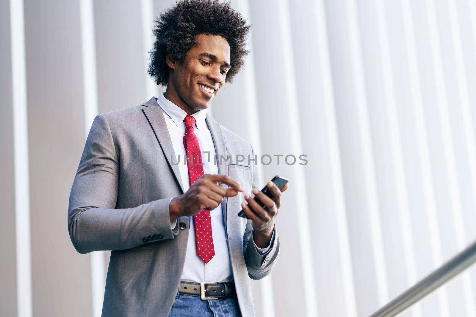 Smiling Black Businessman using his smartphone near an office building. Man with afro hair.