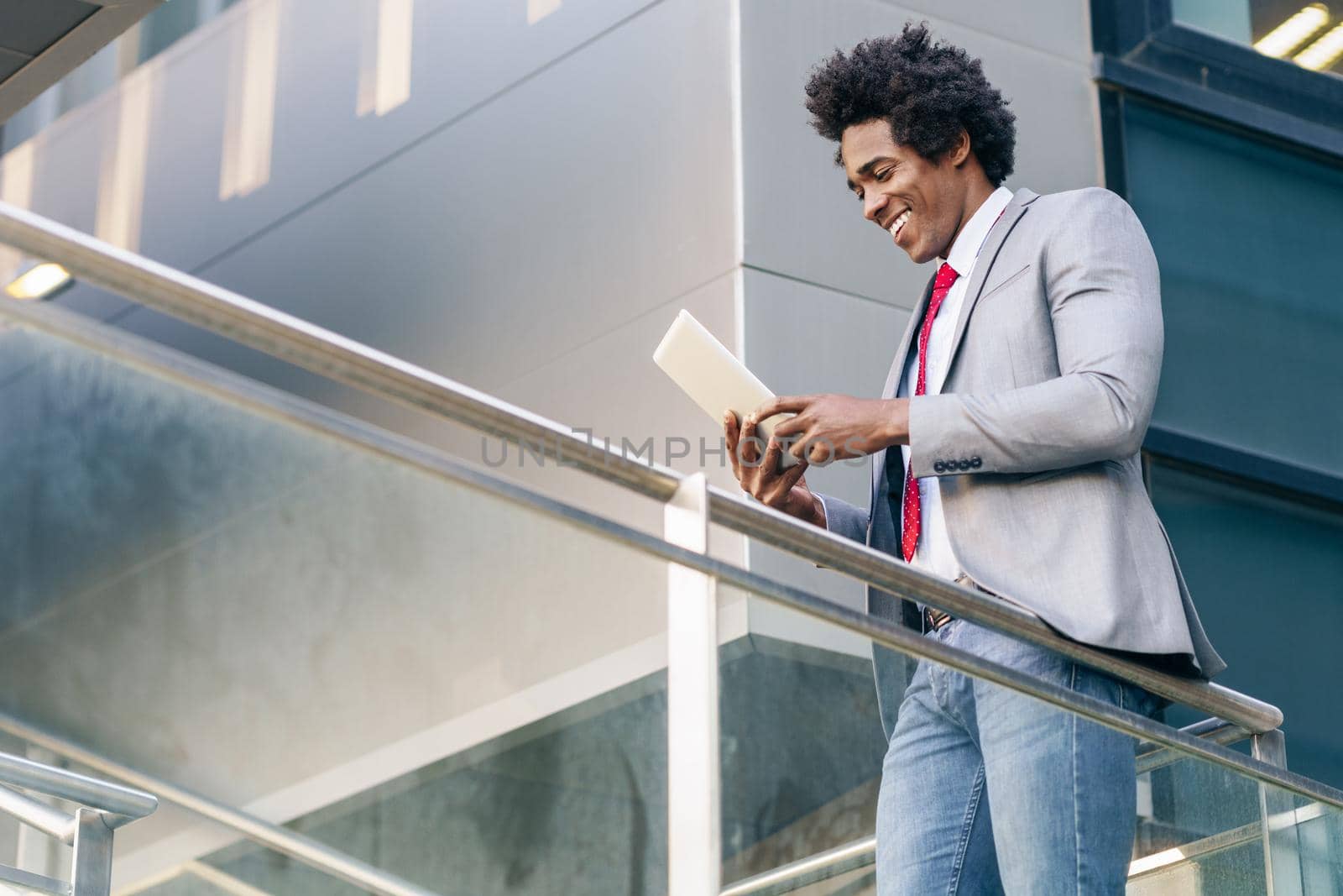 Black Businessman using a digital tablet sitting near an office building. Man with afro hair.