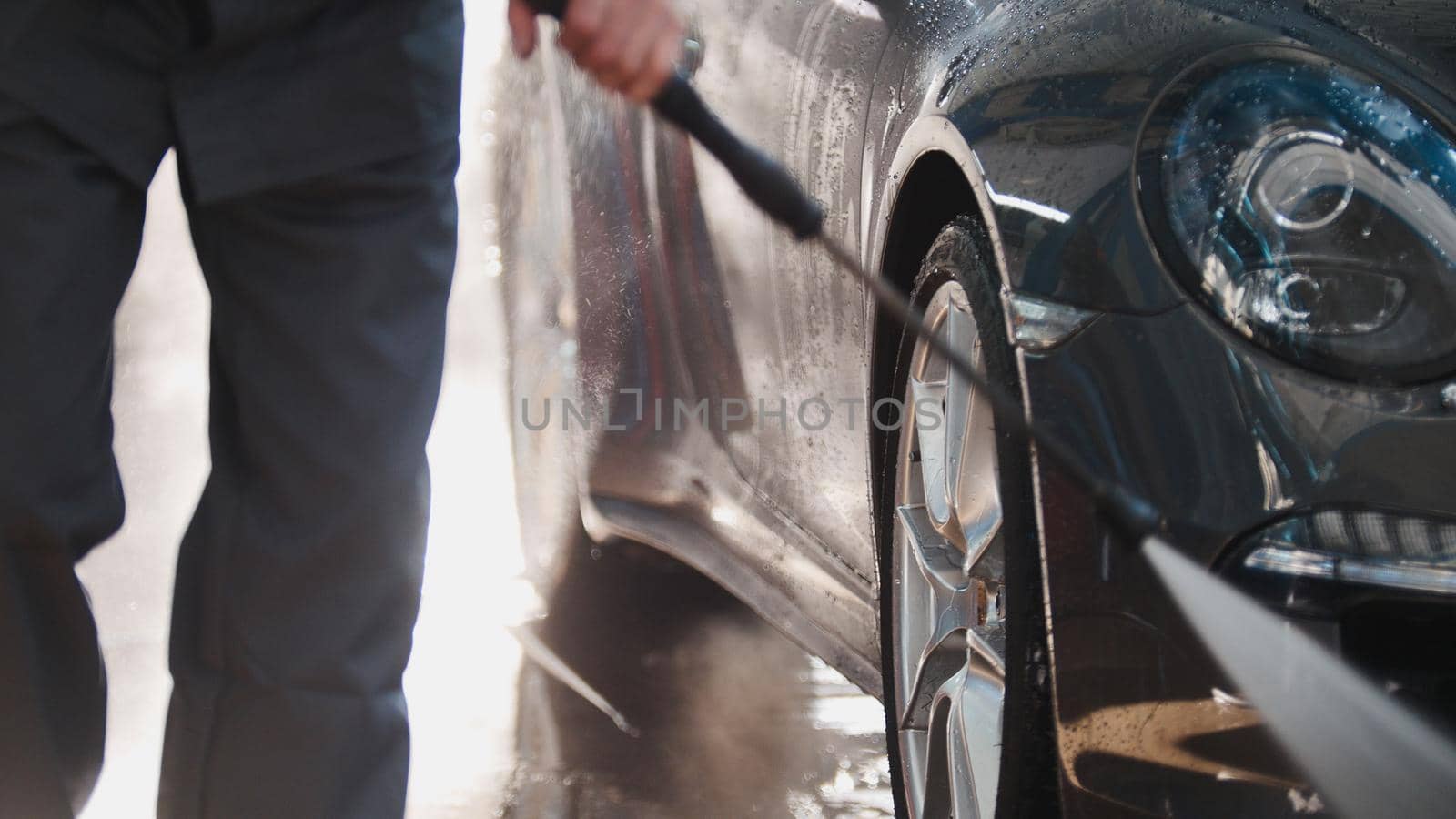 Worker in garage automobile service is washing a car in the suds by water hoses, telephoto, detail close up