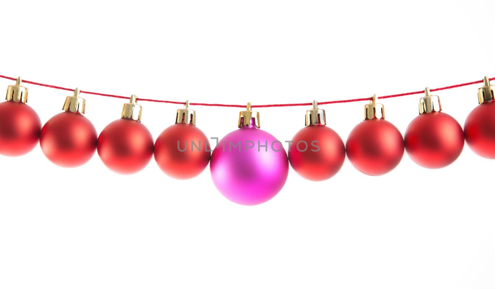 Line of red christmas balls and one lilac or purple ball on white background. Christmas decorations. .
