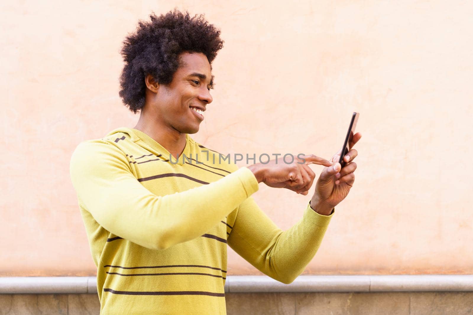 Black man with afro hair and headphones using smartphone in urban background.