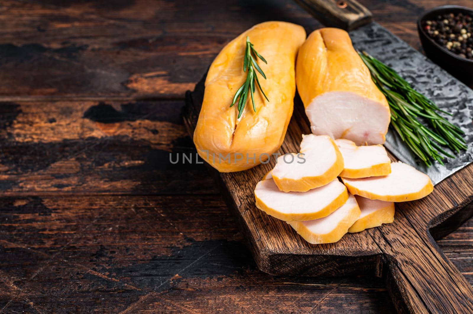 Sliced Smoked chicken breast fillet meat on a butcher board. Dark wooden background. Top view. Copy space by Composter